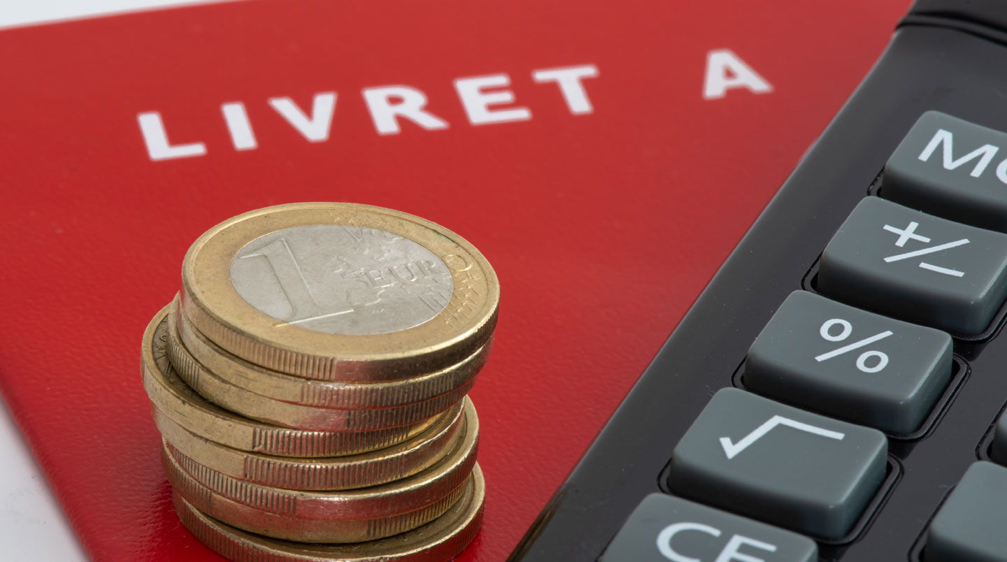 Gros plan sur un livret d'épargne français posé à côté de pièces et billets en euros sur un bureau en bois, faible profondeur de champ